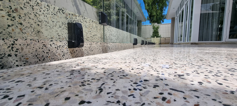 A close-up view of a terrazzo-patterned floor and matching wall in an outdoor architectural setting with glass doors and windows.