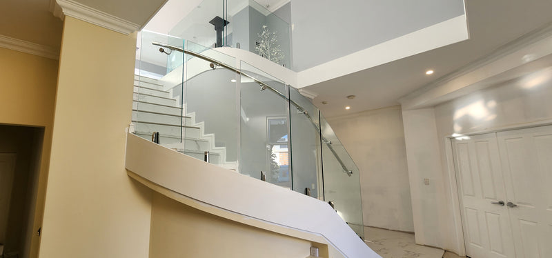 A modern staircase with white steps, a curved white handrail, and clear glass panels, set inside a bright home interior with cream walls and white doors.