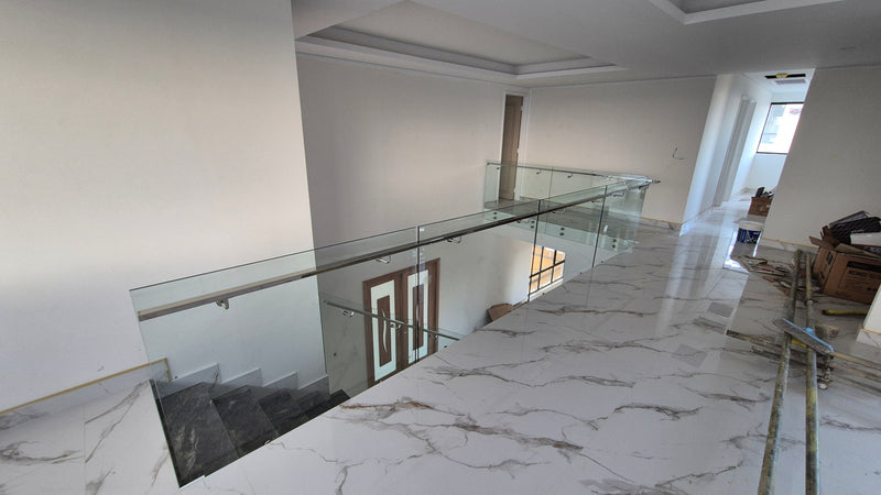 Modern interior staircase and upper landing with a white marble-look railing, glass balustrade, and light-colored walls.