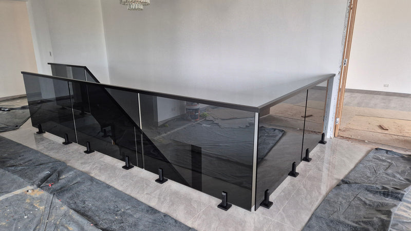 A modern glass and metal staircase railing installed in an unfinished room with gray protective sheeting on the floor.