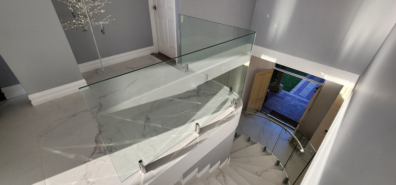Modern glass stair railing installed on a staircase landing, with a marble-tiled floor and gray walls in an interior home setting.