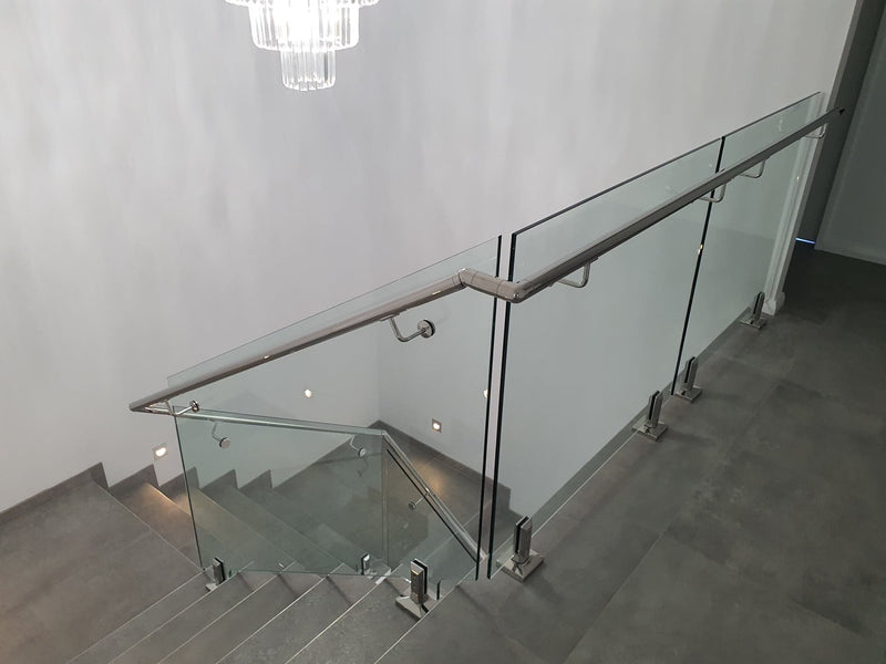 Modern glass stair railing with a brushed metal handrail and transparent glass panels installed on an indoor staircase.