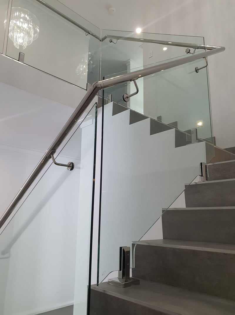 Modern staircase with concrete steps, glass panels, and a brushed metal handrail in a bright interior setting.