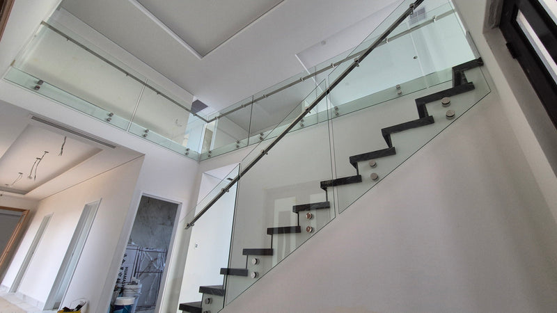 Modern staircase with black steps and clear glass panels, photographed inside a bright residential building.