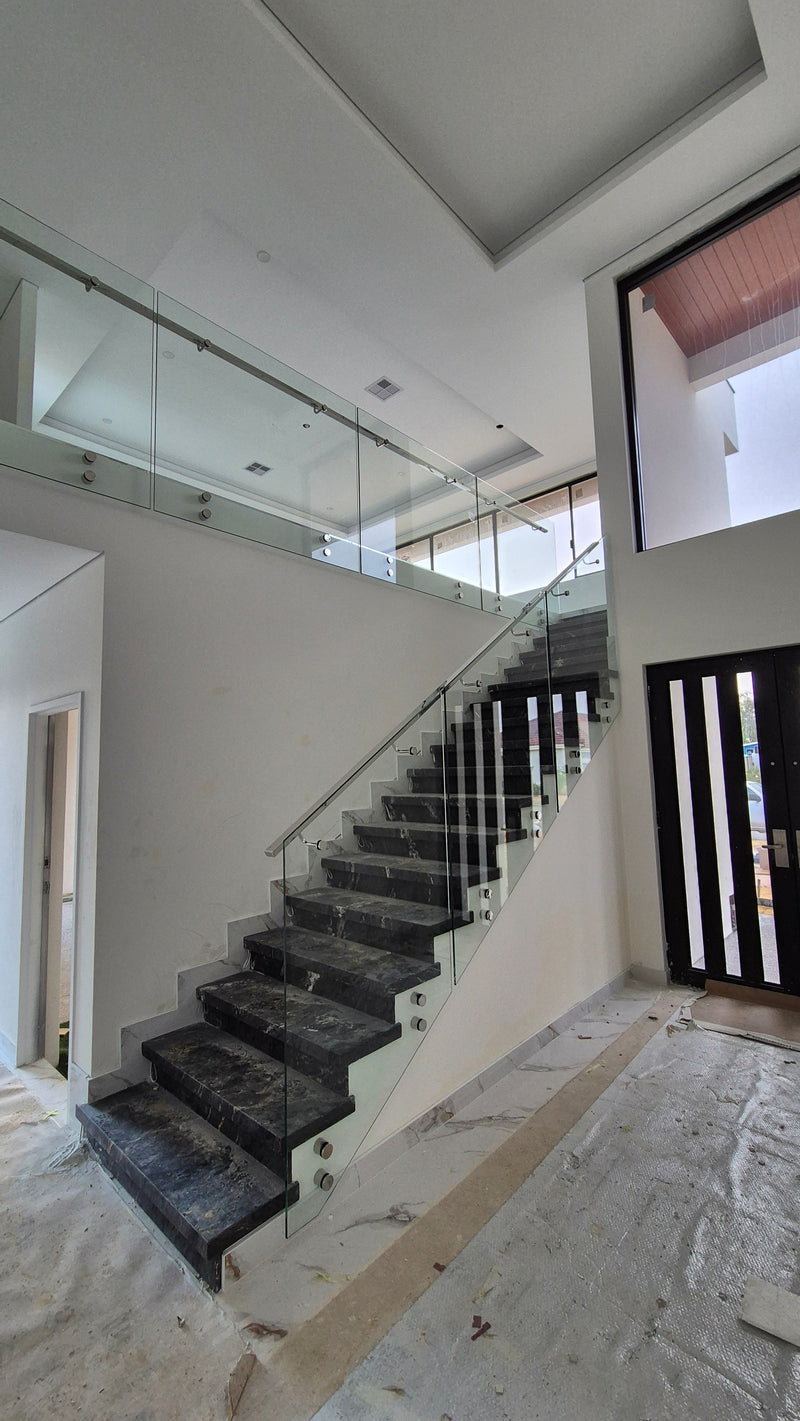 A modern staircase with dark stone steps and clear glass railings inside a bright, white-walled residential building.