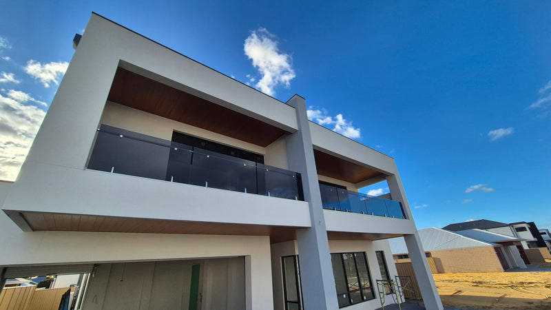 Modern two-story house exterior with white walls, dark glass railings, and a large blue sky background.